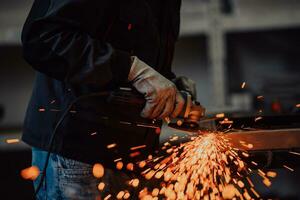 Heavy Industry Engineering Factory Interior with Industrial Worker Using Angle Grinder and Cutting a Metal Tube. Contractor in Safety Uniform and Hard Hat Manufacturing Metal Structures. photo