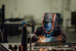 soldador profesional de la industria pesada que trabaja dentro de la fábrica, usa casco y comienza a soldar. enfoque selectivo foto