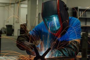 Professional Heavy Industry Welder Working Inside factory, Wears Helmet and Starts Welding. Selective Focus photo