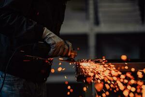 Heavy Industry Engineering Factory Interior with Industrial Worker Using Angle Grinder and Cutting a Metal Tube. Contractor in Safety Uniform and Hard Hat Manufacturing Metal Structures. photo