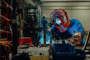 soldador profesional de la industria pesada que trabaja dentro de la fábrica, usa casco y comienza a soldar. enfoque selectivo foto