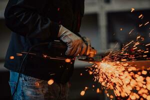 Heavy Industry Engineering Factory Interior with Industrial Worker Using Angle Grinder and Cutting a Metal Tube. Contractor in Safety Uniform and Hard Hat Manufacturing Metal Structures. photo