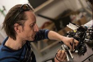 Industrial worker man soldering cables of manufacturing equipment in a factory. Selective focus photo