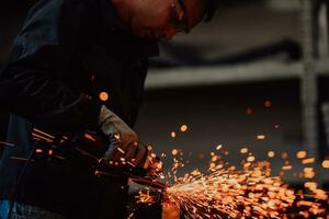 Heavy Industry Engineering Factory Interior with Industrial Worker Using Angle Grinder and Cutting a Metal Tube. Contractor in Safety Uniform and Hard Hat Manufacturing Metal Structures. photo