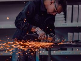 interior de fábrica de ingeniería de industria pesada con trabajador industrial usando amoladora angular y cortando un tubo de metal. contratista en estructuras metálicas de fabricación de cascos y uniformes de seguridad. foto