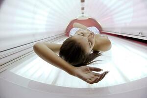 Beautiful young woman tanning in solarium photo