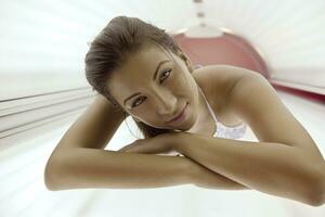 Beautiful young woman tanning in solarium photo