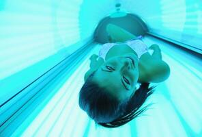 Beautiful young woman tanning in solarium photo