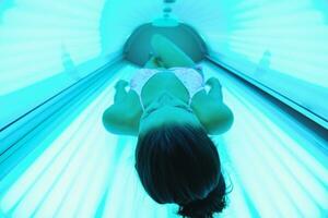 Beautiful young woman tanning in solarium photo