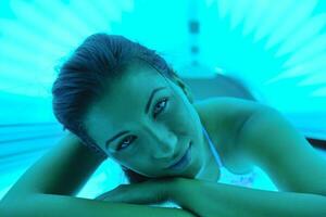 Beautiful young woman tanning in solarium photo