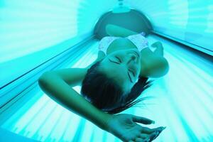 Beautiful young woman tanning in solarium photo