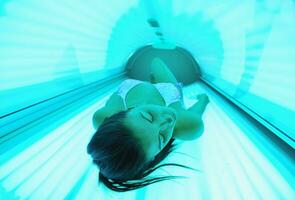 Beautiful young woman tanning in solarium photo