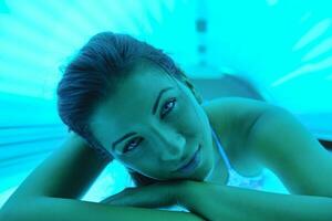 Beautiful young woman tanning in solarium photo