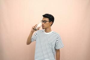 portrait of an asian man wearing glasses wearing a casual striped t-shirt. Enjoying drinking chocolate milk. Isolated beige background. photo