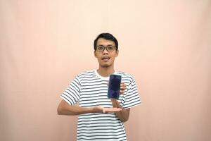 portrait of an asian man wearing glasses wearing a casual striped t-shirt. Shows smartphone screen with happy, surprised, happy expression, for promotion. Isolated beige background. photo