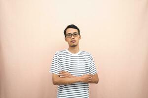 Asian man in glasses wearing casual striped shirt, standing pose with crossed arms, smiling and serious. photo