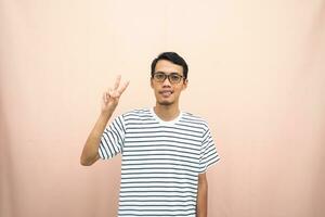 Asian man in glasses wearing casual striped t-shirt, greeting pose and smiling. Isolated beige background. photo