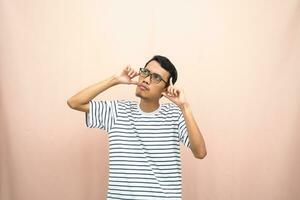 Asian man in glasses wearing casual striped t-shirt, gesturing get ideas, looking for ideas, thinking. Isolated beige background. photo