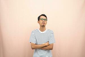 Asian man in glasses wearing casual striped t-shirt, gesturing get ideas, looking for ideas, thinking. Isolated beige background. photo