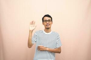 Asian man in glasses wearing casual striped t-shirt, greeting pose and smiling. Isolated beige background. photo
