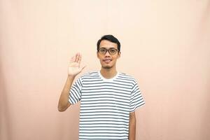 Asian man in glasses wearing casual striped t-shirt, greeting pose and smiling. Isolated beige background. photo