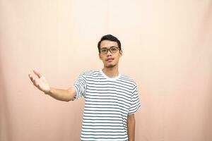 Asian man in glasses wearing casual striped t-shirt, greeting pose and smiling. Isolated beige background. photo