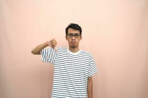 portrait of an asian man in glasses wearing a casual striped t-shirt. denote stop, cross prohibition sign, prohibit something, refuse,. beige background. photo