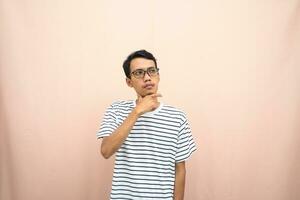 Asian man in glasses wearing casual striped t-shirt, gesturing get ideas, looking for ideas, thinking. Isolated beige background. photo