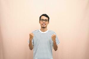 Asian man with glasses wearing casual striped shirt, fist fist pose, indicating strong or ready to fight. Isolated beige background. photo