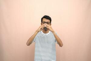 portrait of an asian man wearing glasses wearing a casual striped t-shirt. Enjoying drinking chocolate milk. Isolated beige background. photo