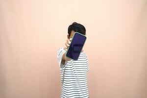 portrait of an asian man wearing glasses wearing a casual striped t-shirt. Shows smartphone screen with happy, surprised, happy expression, for promotion. Isolated beige background. photo