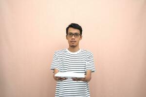 portrait of an asian man in glasses wearing a casual striped t-shirt. bring empty plates. beige background. photo