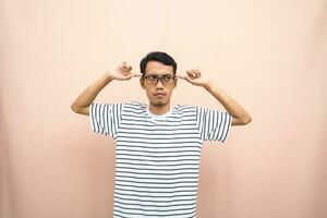 Asian man in glasses wearing casual striped t-shirt, gesturing get ideas, looking for ideas, thinking. Isolated beige background. photo