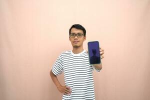 portrait of an asian man wearing glasses wearing a casual striped t-shirt. Shows smartphone screen with happy, surprised, happy expression, for promotion. Isolated beige background. photo