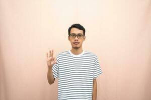 Asian man in glasses wearing casual striped shirt, posing giving thumbs up gesture or okay that agree. Isolated beige background. photo