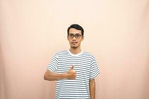 Asian man in glasses wearing casual striped shirt, posing giving thumbs up gesture or okay that agree. Isolated beige background. photo