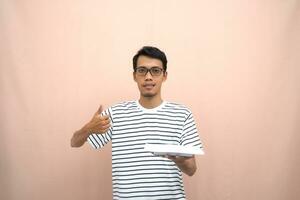 portrait of an asian man in glasses wearing a casual striped t-shirt. bring an empty plate with a thumbs up if you like or agree. beige background. photo