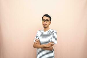 Asian man in glasses wearing casual striped shirt, standing pose with crossed arms, smiling and serious. photo