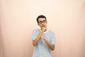 Asian man in glasses wearing casual striped t-shirt, gesturing get ideas, looking for ideas, thinking. Isolated beige background. photo