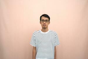 portrait of an asian man wearing glasses wearing a casual striped t-shirt. Stand up straight. Isolated beige background. photo