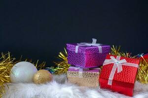 regalo cajas en parte superior de cada otro con Navidad pelotas y Navidad oropel. rojo, oro y púrpura cajas Navidad tarjeta. Copiar espacio en parte superior en un oscuro antecedentes. foto