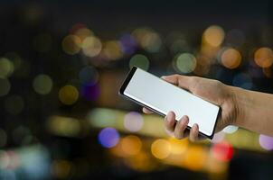 men or women hands holding on smartphone blank white screen at night colorful bokeh  background. photo