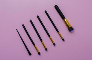 set makeup brushes on pink or purple colored composed background. Top view photo