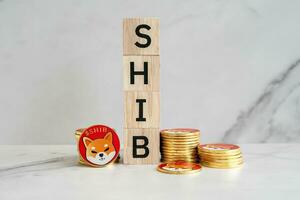 Many of Shiba inu coins SHIB are placed vertically next to a wooden block in the center with a white marble background. photo