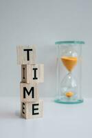 Wooden blocks with the word TIME written on it, against the background of an hourglass and white background. photo