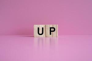 Wooden blocks form the text UP against a pink background. photo