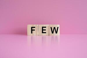 Wooden blocks form the text FEW against a pink background. photo