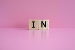 Wooden blocks form the text IN against a pink background. photo