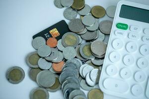 1 black credit card covered with many baht coins with a calculator next to it with a white background. photo