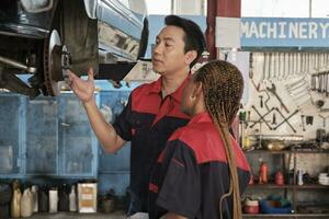 Professional automotive supervisors inspect and discuss car suspension repair work with female African American mechanic worker at service garage, and fix specialist occupations in the auto industry. photo